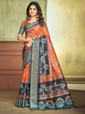 A woman modeling a traditional Indian saree with a vibrant orange and black patterned body, teal borders, and a matching teal blouse, set against a warm beige and brown studio background.